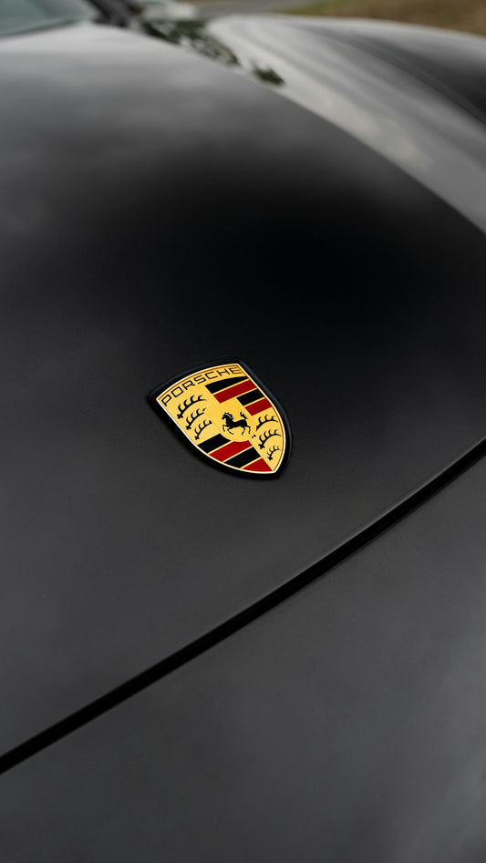 A porsche emblem rests on a black car.